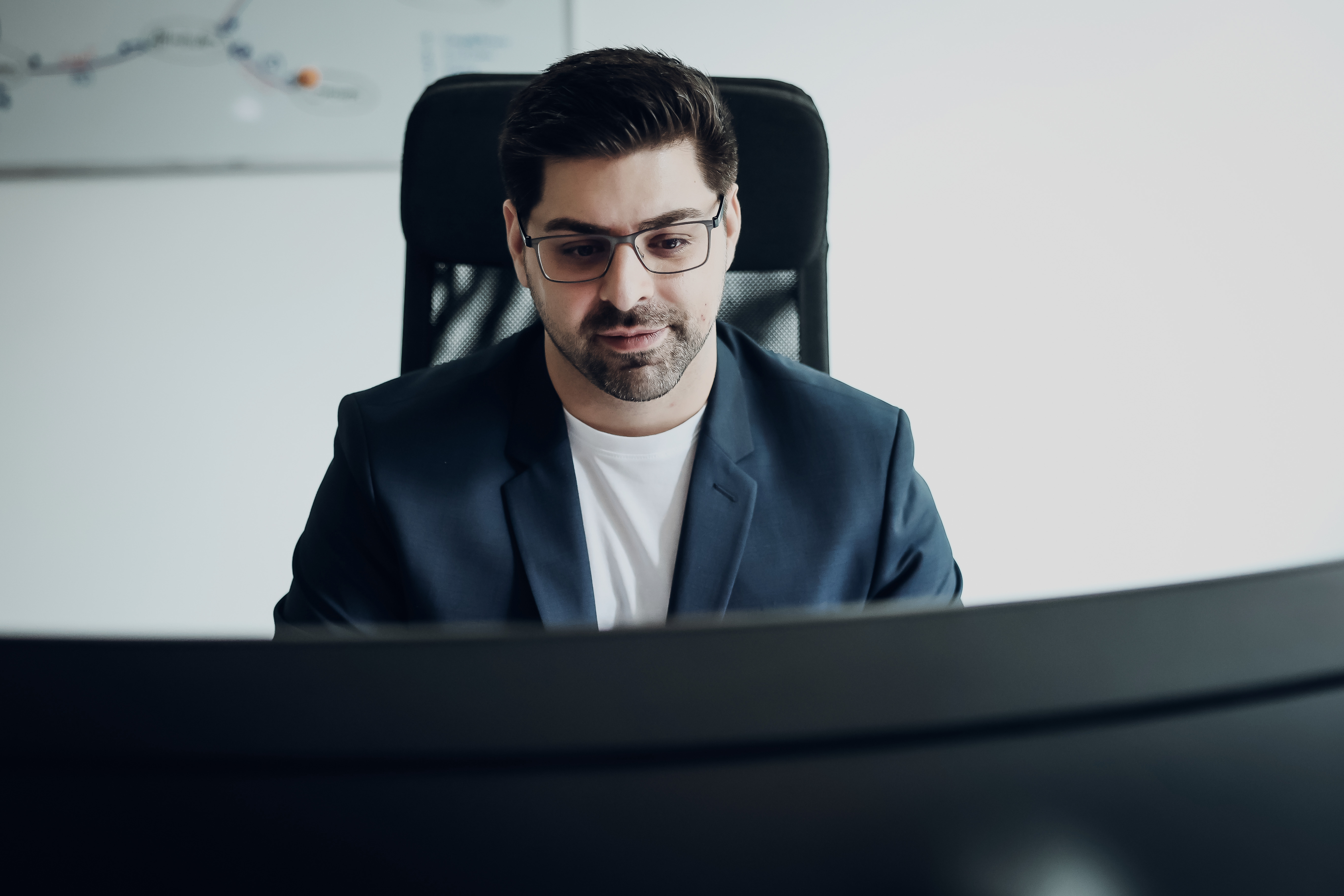 Mann mit Brille arbeitet konzentriert an einem großen Monitor in einem modernen Büro.