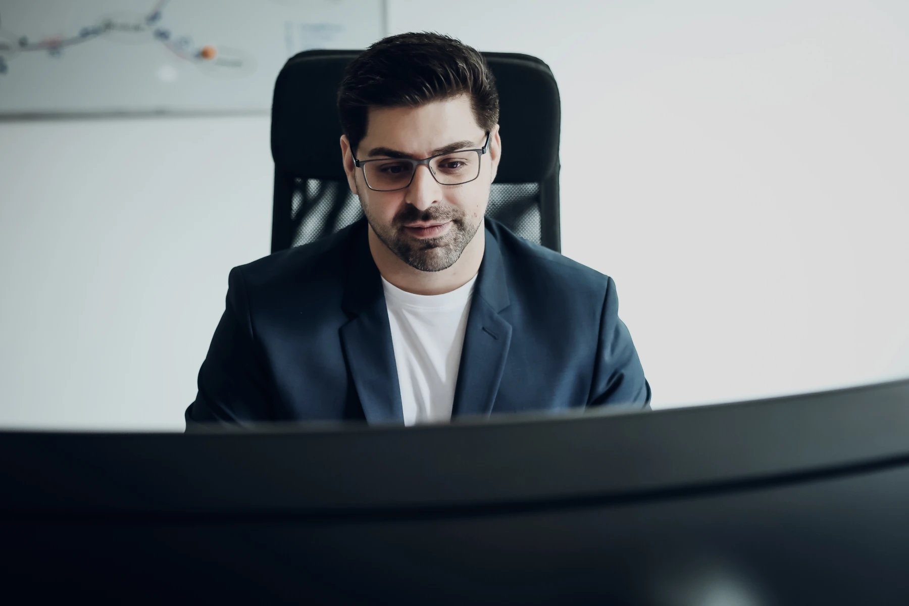 Mann mit Brille arbeitet konzentriert am großen Monitor in einem Büro.