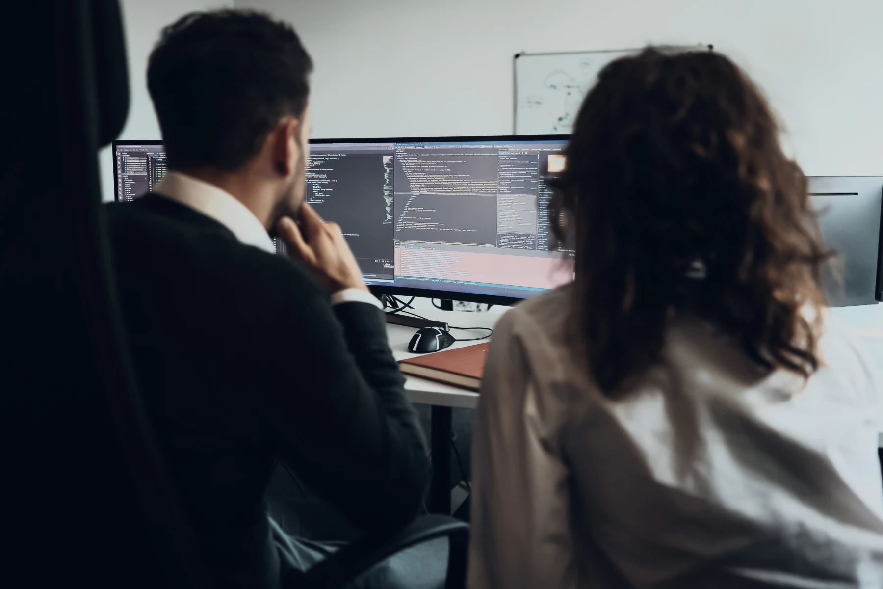 Zwei Personen arbeiten im Büro gemeinsam an Monitoren mit Programmcode.