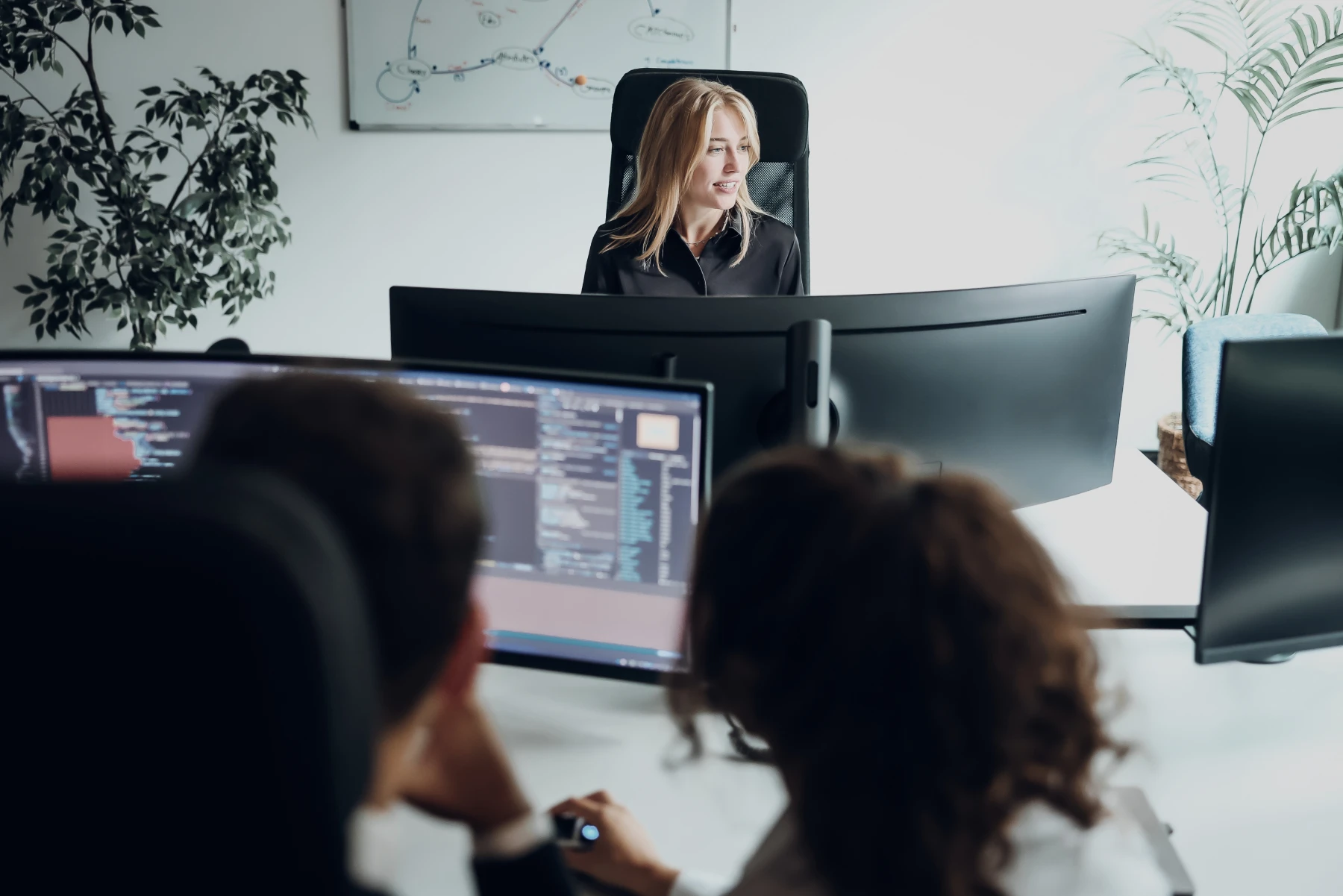 Team in einem hellen Büro arbeitet an mehreren Monitoren mit Codeansichten.